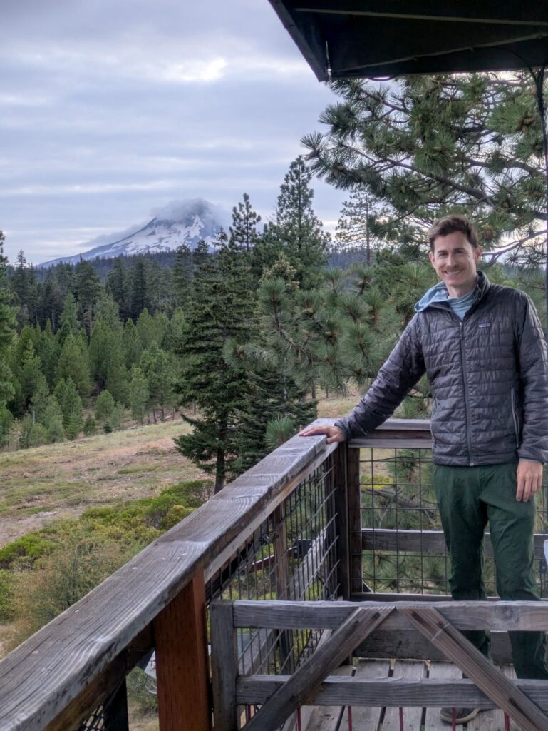 Man on lookout tower porch with mountain in background